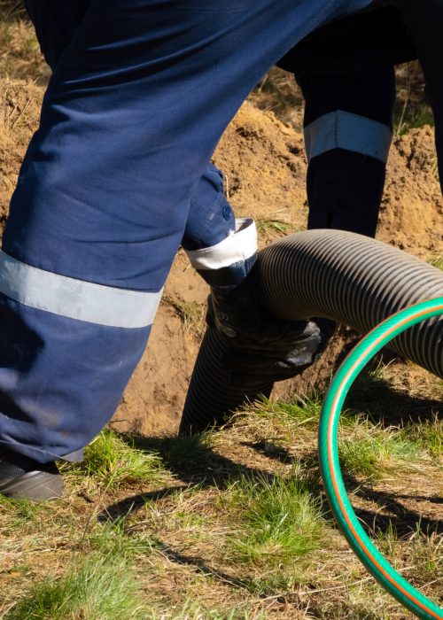 Man worker holding pipe, providing sewer cleaning service outdoor. Sewage pumping machine is unclogging blocked manhole